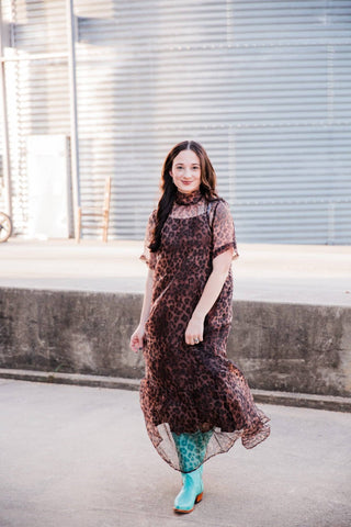 Model walking in the Sable Leopard Maxi Dress with a flowing sheer ruffle hem and turquoise Western boots.
