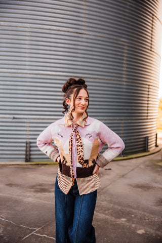 Sadie wearing the Sunset Cowboy Cardigan with a desert scene and horse silhouettes, hands on hips over a striped blouse.