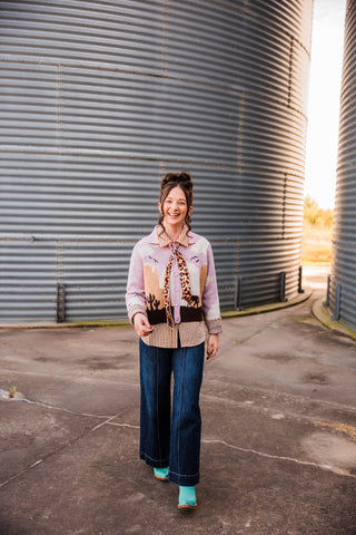 Sadie walking in the Sunset Cowboy Cardigan, styled with a striped blouse, leopard-print neck scarf, wide-leg jeans and teal boots.