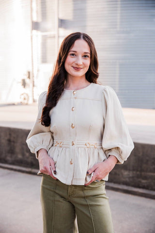 Sadie wearing the cream Sutton Top with olive pants, showing its round neckline, puff sleeves and peplum hem.