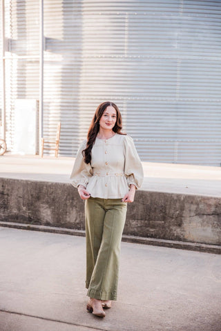 Sadie styling the cream Sutton Top with olive wide-leg pants and neutral ankle boots beside a metal grain bin.