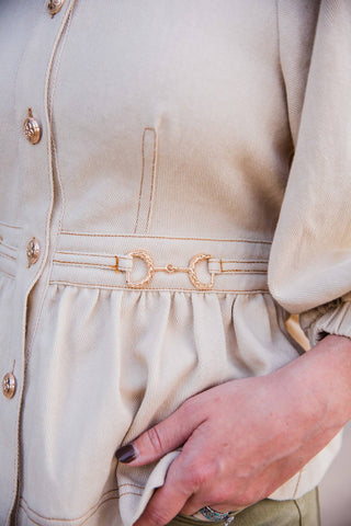 Close-up of the Sutton Top’s gold-tone equestrian-inspired waist accent, contrast stitching and gathered cream denim.