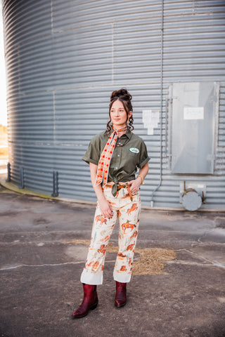 Sadie wearing the cream Cowboy Way Pants with an olive knotted shirt, printed neck scarf, leather belt and burgundy boots.