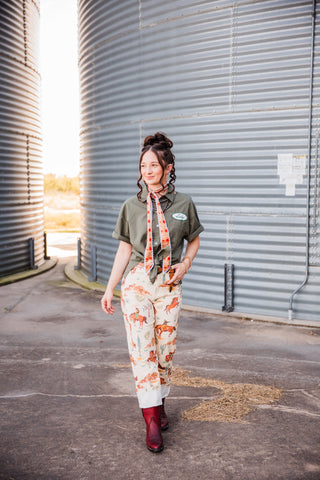 Sadie walking in the cream Western-print Cowboy Way Pants with rolled cuffs, styled with an olive shirt and burgundy boots.