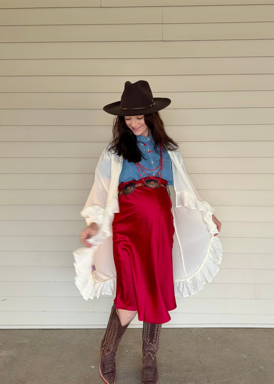 Person wearing a cowboy outfit with a hat, red skirt, and white shirt against a neutral background