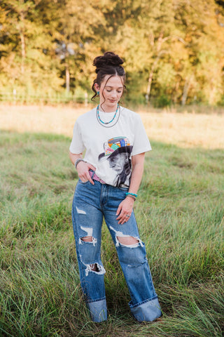 Sadie wearing blue Roper wide-leg jeans with distressed knees and cuffed hems, styled with a graphic tee and pink belt.