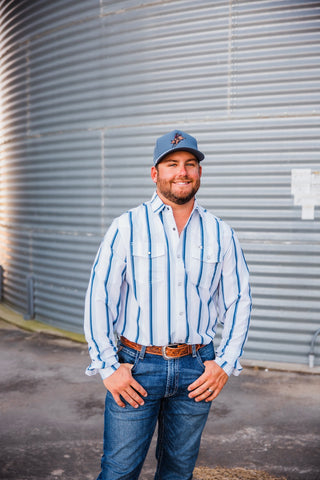 Trevor wearing the Tristan pearl snap with blue vertical stripes and two chest pockets, tucked into jeans with a leather belt.
