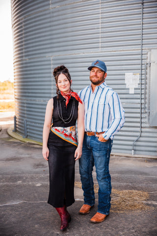 Trevor wearing the blue-striped Tristan pearl snap with jeans and brown boots, standing beside Sadie in a black dress.