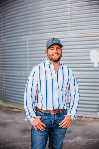Front view of Trevor in the blue-striped Tristan long-sleeve pearl snap, styled with jeans, a tooled leather belt and blue cap.