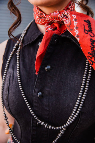 Close-up of the black denim Walk the Line Dress collar and snap-front bodice, styled with a red scarf and layered necklaces.