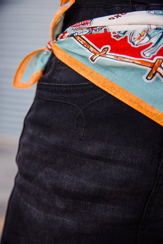 Close-up of curved stitching at the hip of the black denim Walk the Line Dress beneath a colorful printed waist scarf.