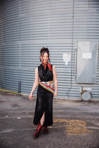 Sadie modeling the black denim Walk the Line Dress with a front slit, red Western boots and a printed waist scarf.