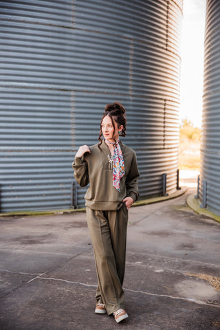Sadie styling the olive Weekend Trail Knit Set with a printed neck scarf and sneakers, one hand raised to her shoulder.