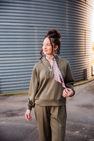 Closer view of the olive Weekend Trail half-zip pullover with a stand collar, styled with a printed scarf and silver jewelry.