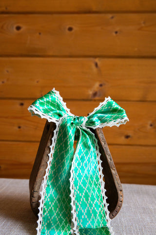 Adorned silk twilly by Allie Falcon tied in a bow, showing a green and white geometric print with white crochet trim.