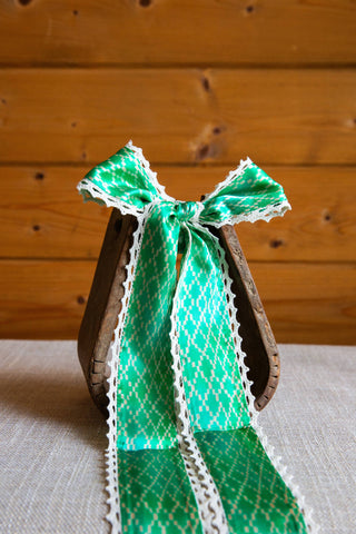 Allie Falcon Adorned silk twilly displayed in a bow with long green geometric-print tails and scalloped white crochet edges.