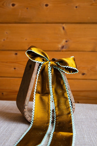 Esther silk twilly by Allie Falcon tied in a bow, showing golden brown fabric with a subtle print and pale mint crochet trim.