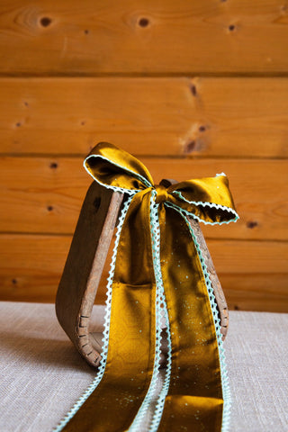 Allie Falcon Esther silk twilly draped from a bow, featuring long golden brown tails and contrasting mint crochet edges.