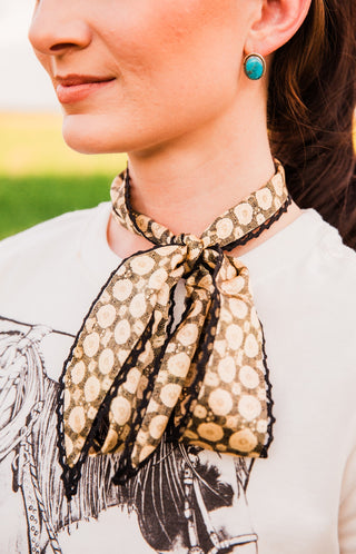 Josephine Twilly bow detail with black crochet trim outlining cream doily-patterned loops and pointed tails over a graphic tee.