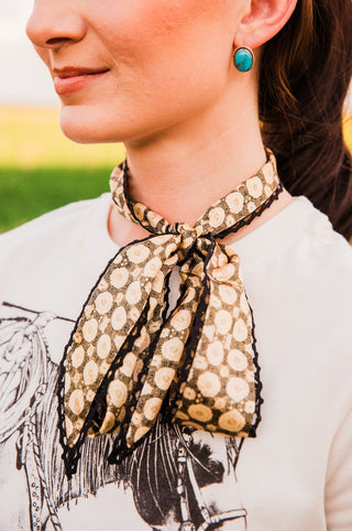 Close-up of the Josephine Twilly neck scarf with cream circular doily print, pointed ends and scalloped black crochet edging.