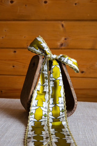 Mod Maud silk twilly by Allie Falcon showing repeating white hat-wearing profiles on yellow fabric with olive crochet trim.