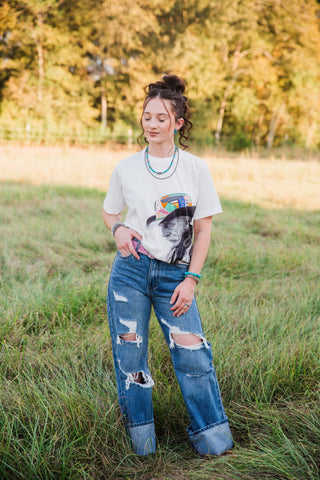 Allie Falcon Reverie Tee in white with cowboy artwork, styled tucked into distressed blue jeans for a western casual outfit.