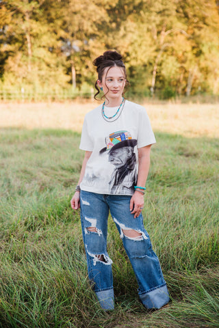 Full-length view of the white Allie Falcon Reverie Tee, showing its relaxed boxy fit and cowboy graphic with ripped jeans.