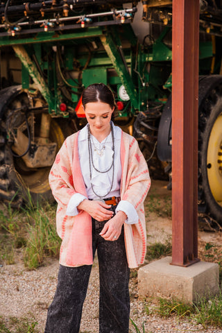 Model adjusting white blouse cuffs beneath the Winnie Boyfriend Cardigan, showing its loose sleeves and pink inner edge.
