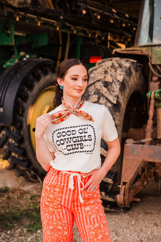 Winnie Twilly with white decorative edging tied above a cream graphic tee, adding a peach and orange floral accent to the outfit.