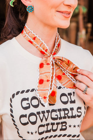 Close-up of a model holding the Winnie Twilly bow, highlighting orange-red flowers, peach patterned fabric and white wavy edging.