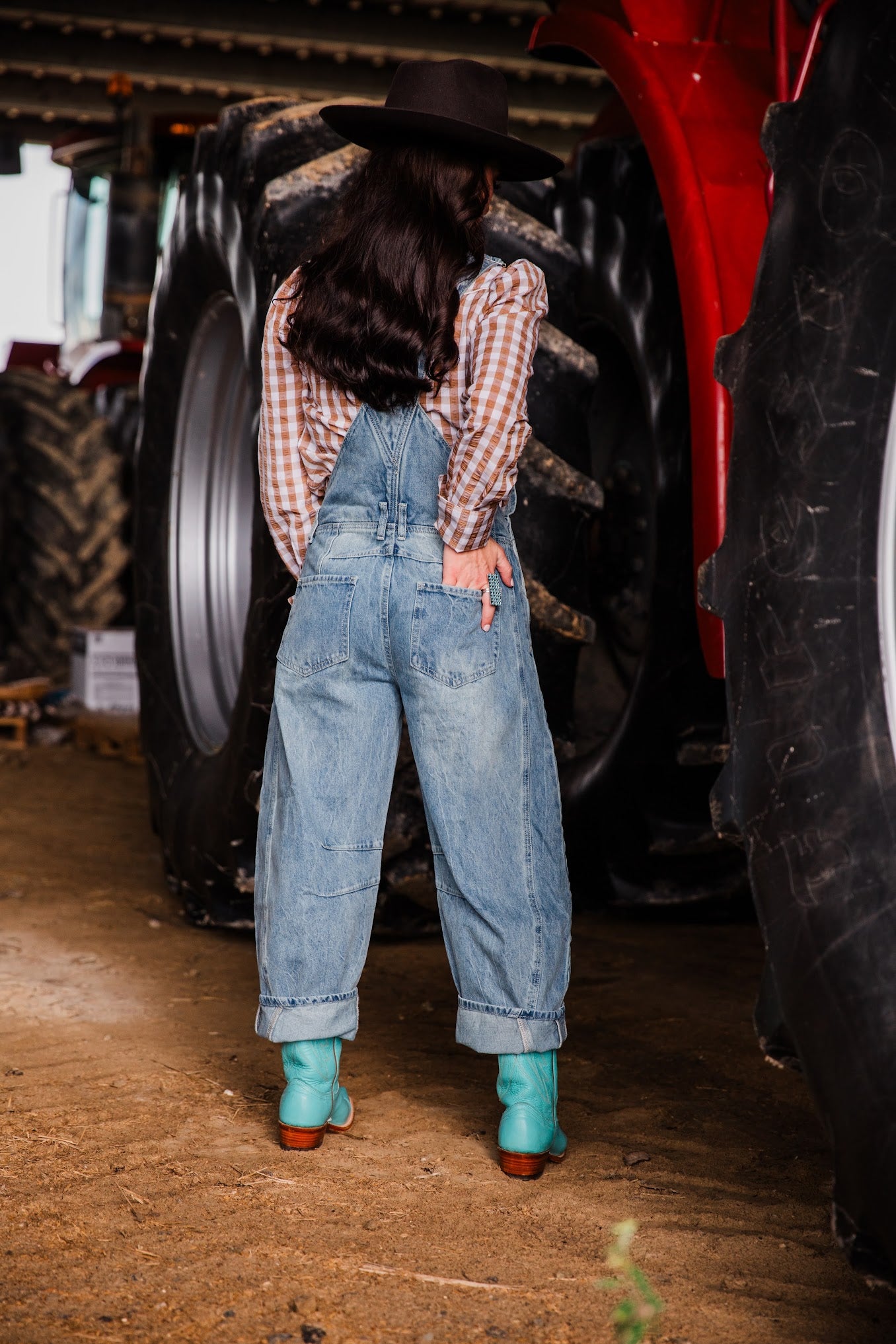 Back view of women’s light wash denim overalls with oversized barrel legs and back pockets