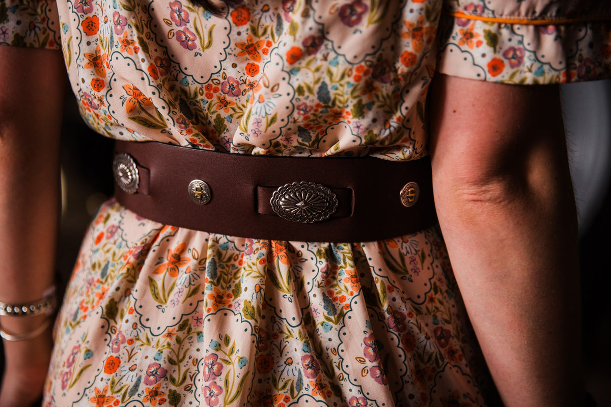Briar Lee Western concho belt styled over a women’s floral midi dress with cowboy boots