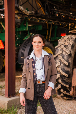 Front view of the Bonnie brown concho belt with an oval silver-tone centerpiece, worn with black jeans and an open Western blazer.