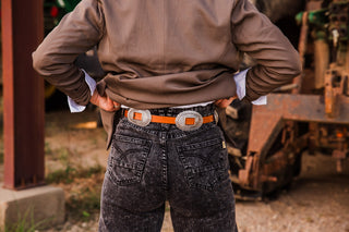 Bonnie Concho Belt across the back waist of black jeans, showing a narrow brown strap threaded through oval silver-tone conchos.