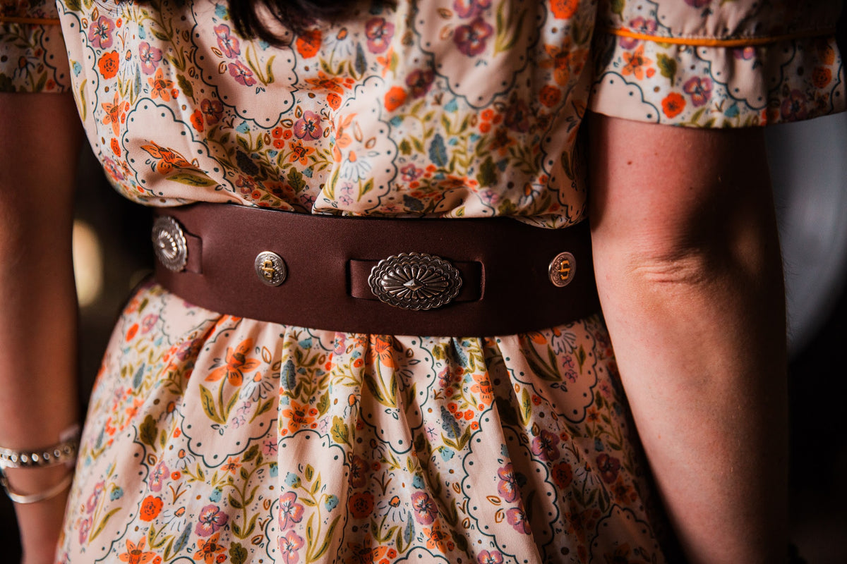 Close-up of dark brown leather cowgirl belt with silver-tone Western concho detailing