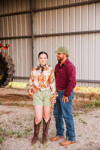 Bronco Boot Top in cream and orange worn with green shorts and a neck scarf, pictured with a man outside a metal barn.