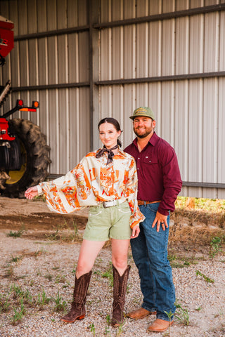 Model wearing the cream and orange Bronco Boot Top with green shorts and cowboy boots beside a man in a maroon shirt.