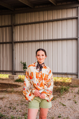 Front view of the Bronco Boot Top with an allover cream and orange Western print and loose long sleeves, worn with shorts.