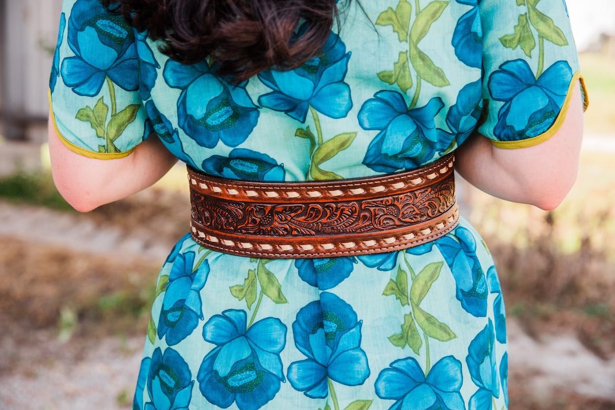 Rear close-up of the Brown Vintage Buck Stitched Belt with cream lacing framing dark floral tooling over a blue floral dress.