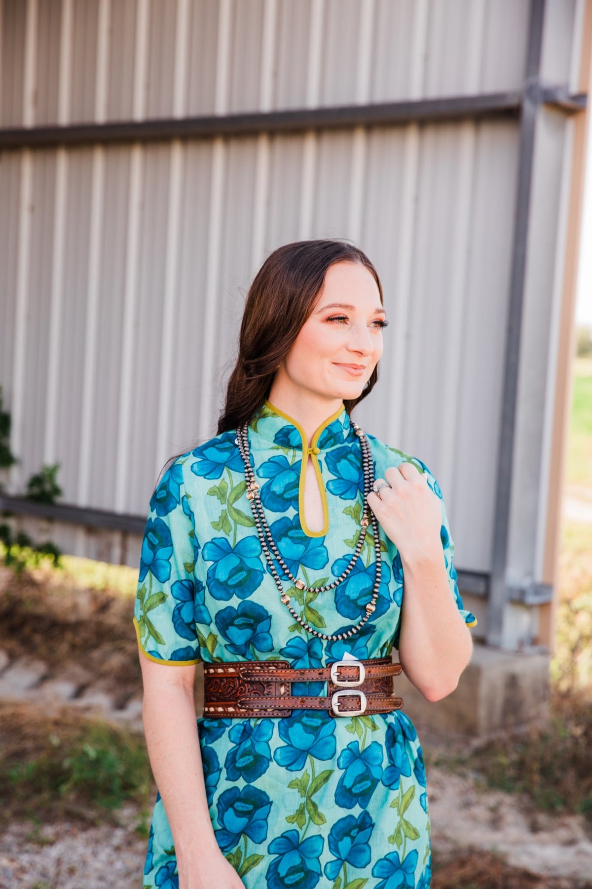Brown Vintage Buck Stitched Belt styled at the waist of a blue floral dress with layered silver-tone bead necklaces.