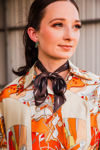 Buckstitch Brown Twilly by Fringed Scarves tied in a neck bow, showing cream buckstitch motifs on a dark brown background.