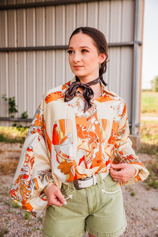 Buckstitch Brown Twilly worn as a bow above an orange and cream Western print blouse, styled with olive shorts and a white belt.