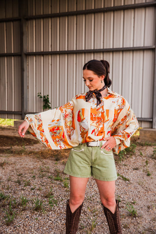 Buckstitch Brown Twilly neck scarf styled with a wide-sleeve Western blouse, olive denim shorts and tall brown cowboy boots.