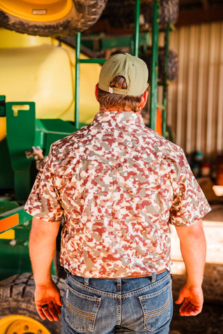 Back view of the Camo Lite short sleeve pearl snap shirt, showing its Western yoke and allover camouflage print tucked into jeans.