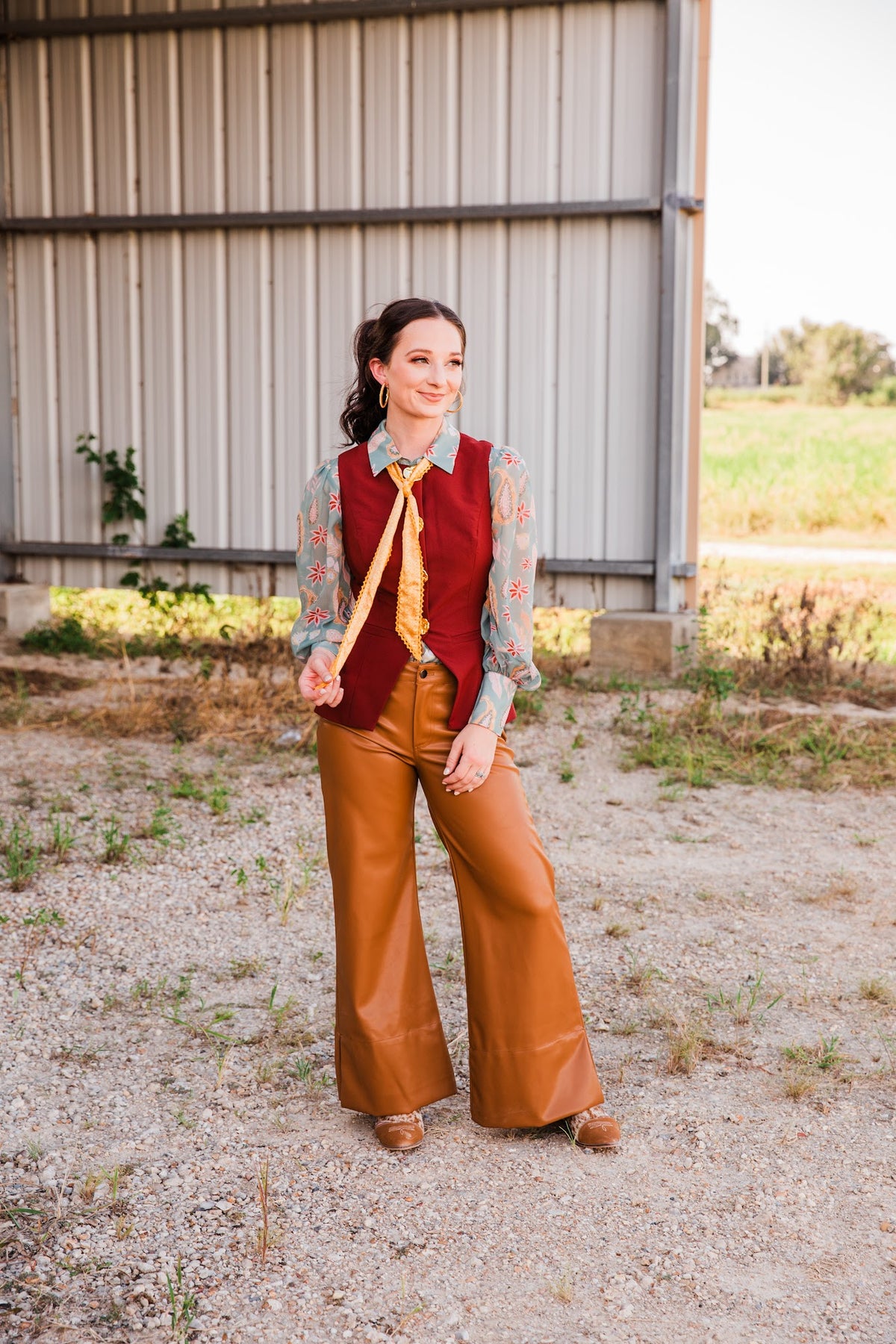 Full-length look at the burgundy Carmen Vest styled with a sage paisley blouse, yellow neck scarf and caramel wide-leg pants.
