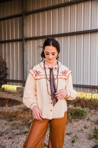 Chocolate Twilly tied at the neck of a cream embroidered blouse, with long brown ends draped between layered necklaces.
