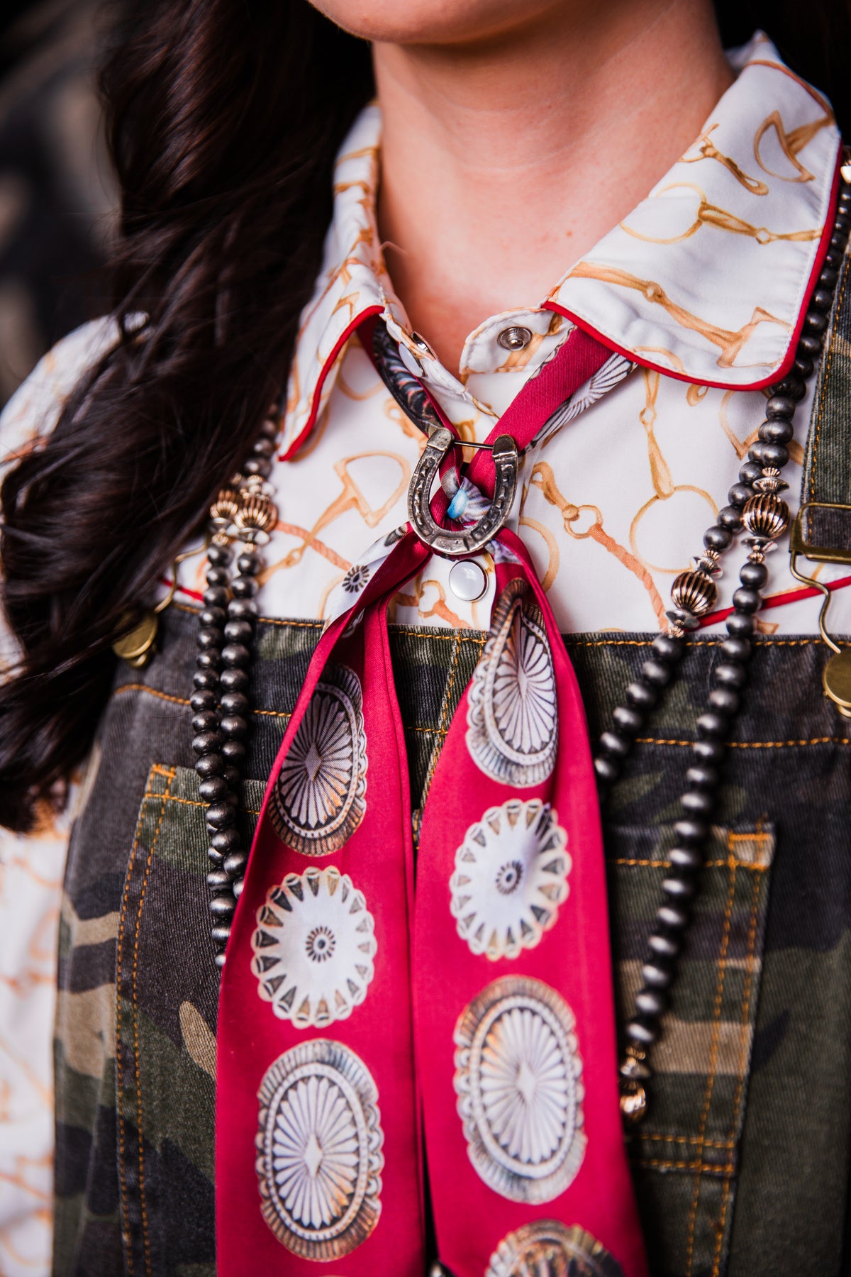 close up view of big concho red twilly by fringed scarves styled with horseshoe scarf slide