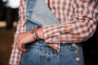 Close-up of women’s brown gingham Western pearl snap shirt with piping and snap cuff details