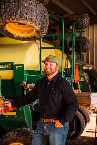 Front view of the CORE Black long sleeve pearl snap shirt with two flap chest pockets, worn with jeans beside farm equipment.