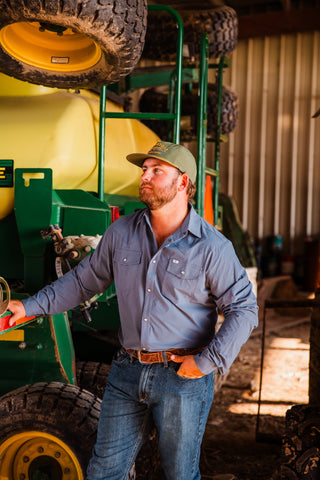 Model wearing the solid CORE Blue long sleeve pearl snap shirt in a barn, showing the pointed collar and white snaps.